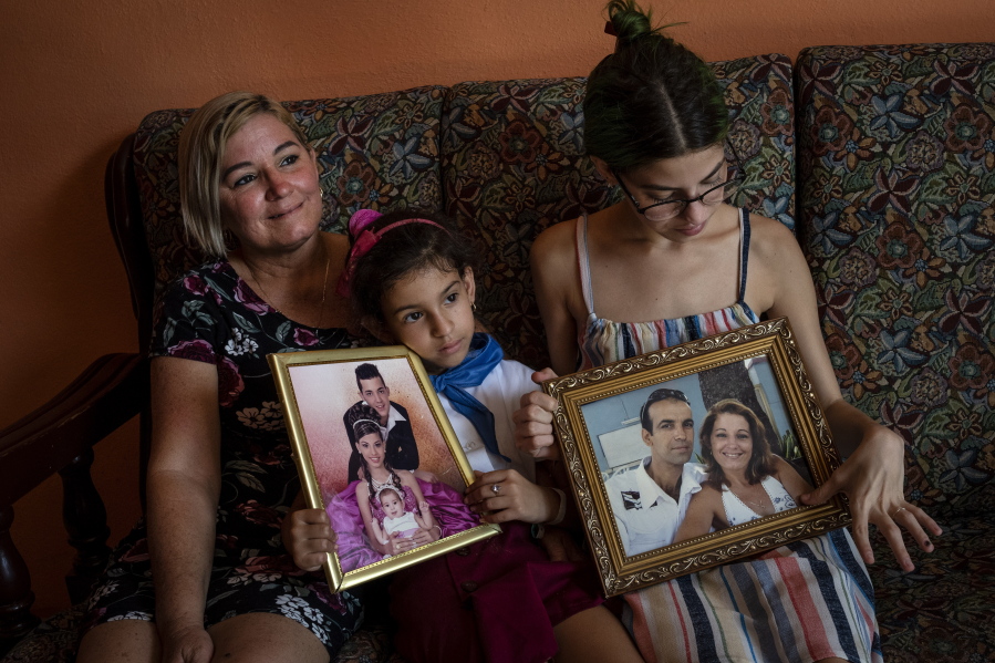 Danmara Triana, left, with her daughters Alice, center, and Claudia, show photos of them with their brother and father who moved to the United States in 2015, at their home in Cienfuegos, Cuba, Thursday, May 19, 2022. Separated families see hope in the measures announced by the U.S. administration of President Joe Biden, but the long wait of years and a web of political interests also makes them skeptical.