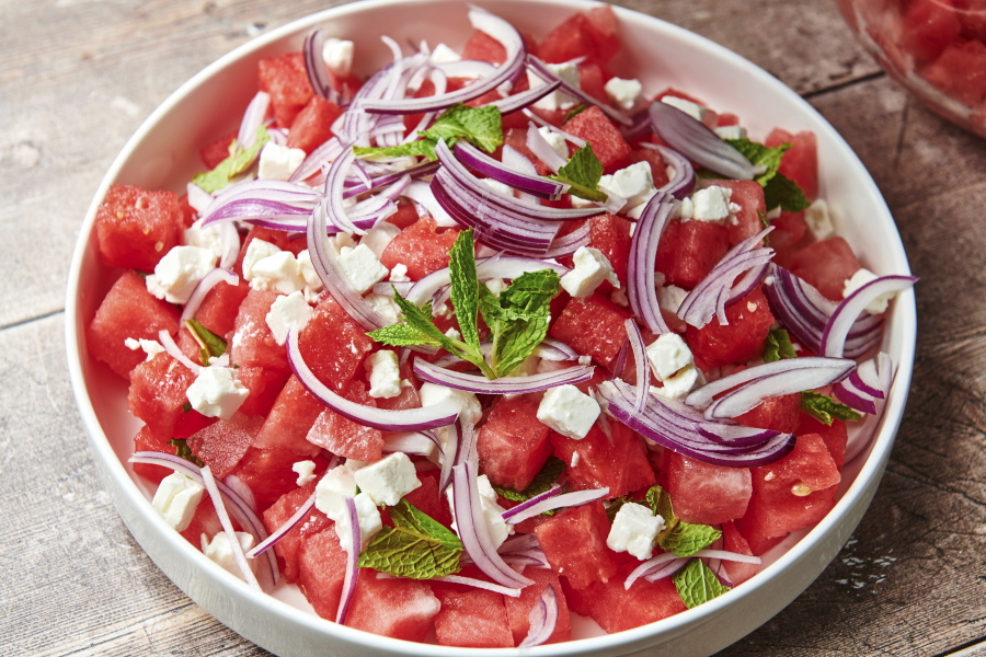 This image shows a recipe for watermelon feta salad topped with thinly sliced red onion and mint leaves.