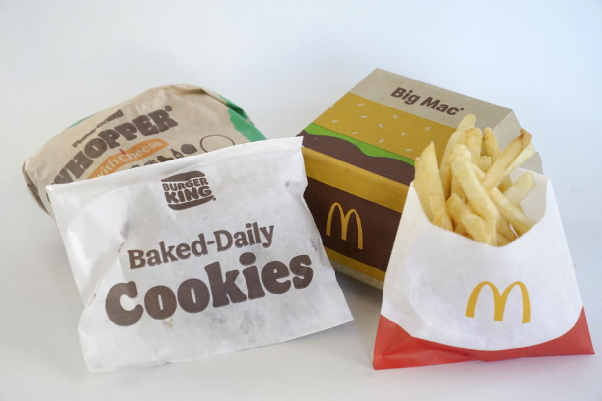 A Burger King Whopper in a wrapper, behind left, and a bag of Burger King cookies, left, rest next to a McDonald's Big Mac in a container, behind right, and a bag of McDonald's fries, in Walpole, Mass., Wednesday, April 20, 2022. Environmental and health groups are pushing dozens of fast food companies, supermarkets chains and other retail outlets to remove PFAS from their packaging.