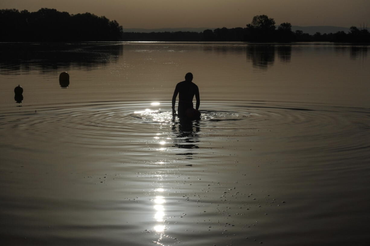 FILE - A man walks in the water as the sun rises above the Miribel lake, outside Lyon, central France, Saturday, June 18, 2022. A heat wave that's already lasted more than a week keeps on baking the US, Asia, Europe and even the Arctic.