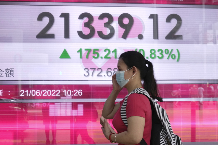 A woman wearing a face mask walks past a bank's electronic board showing the Hong Kong share index in Hong Kong, Tuesday, June 21, 2022. Asian stocks rebounded Tuesday as Wall Street futures moved higher while U.S. markets were closed for a holiday.