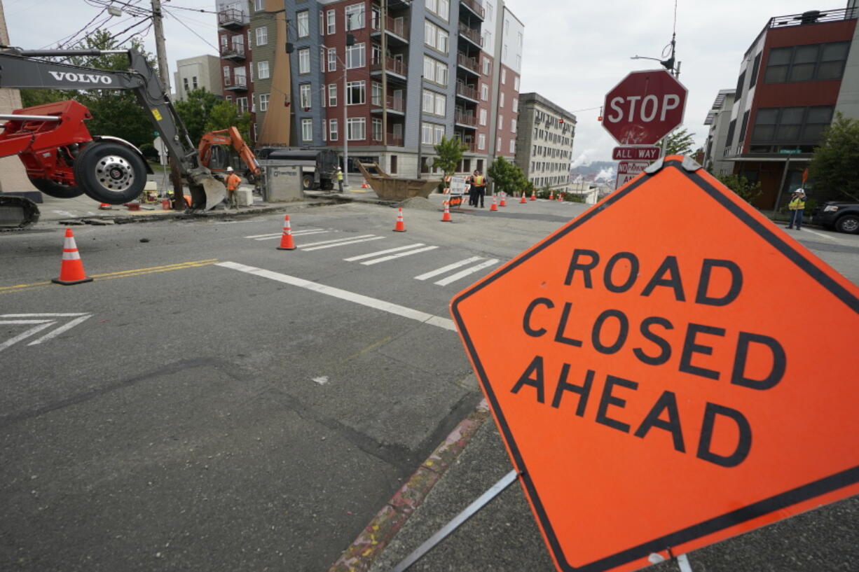 A sign is shown near ongoing work on a project to replace water main pipes, Wednesday, June 15, 2022, in downtown Tacoma, Wash. Inflation is taking a toll on infrastructure projects across the U.S., driving up costs so much that state and local officials are postponing projects, scaling back others and reprioritizing their needs. (AP Photo/Ted S.