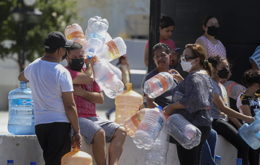 Neighbors wait with plastic containers in hand to collect water at a public collection point in Monterrey, Mexico, Monday, June 20, 2022. Local authorities began restricting water supplies in March, as a combination of an intense drought, poor planning and high use has left the three dams that help supply the city dried up, with thousands of homes not receiving any water for weeks.