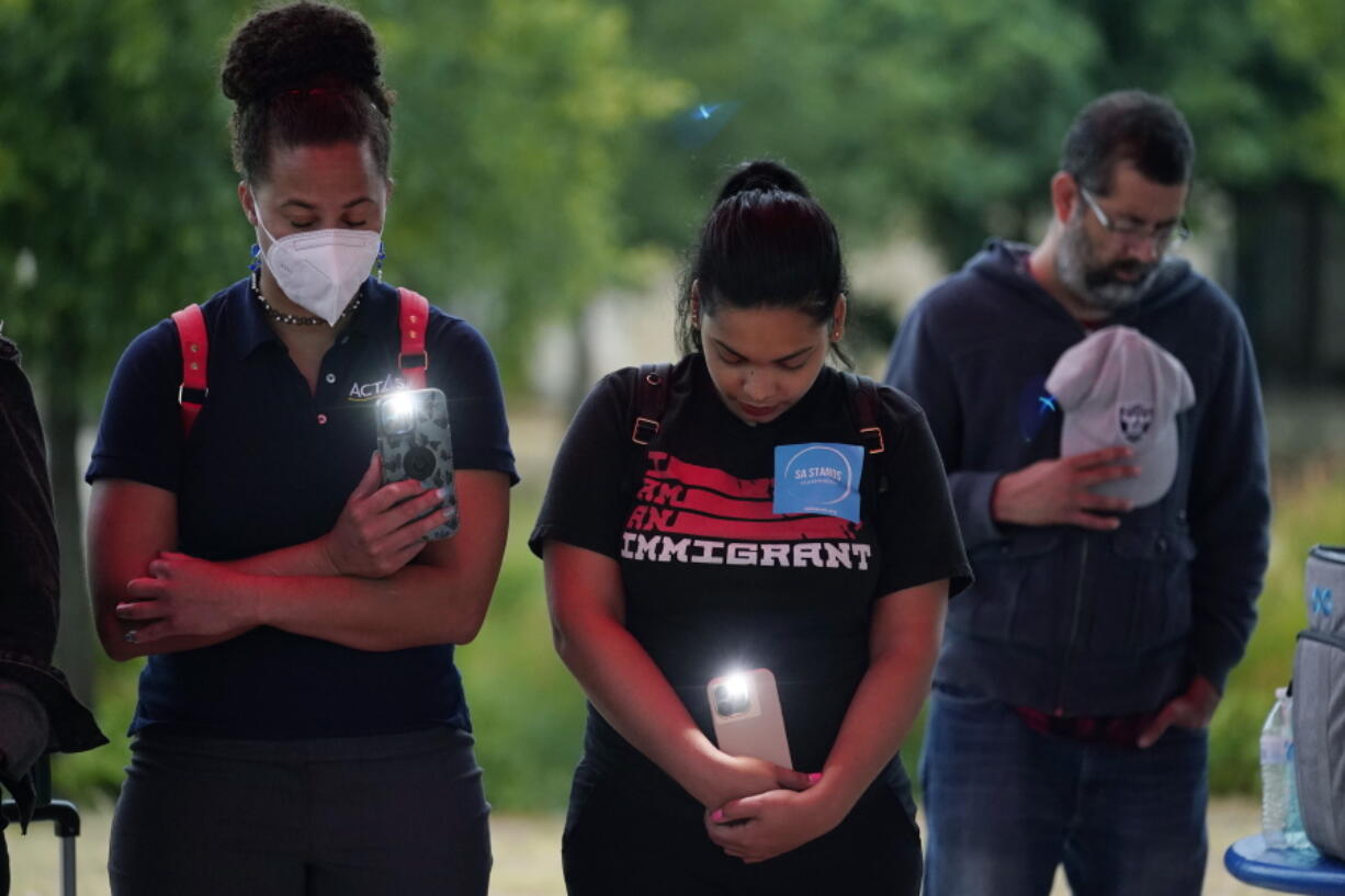 Naiyolis Paloma, center, prays with others during a community vigil for the dozens of people found dead Monday in a semitrailer containing suspected migrants as well as those who received heat related injuries, Tuesday, June 28, 2022, in San Antonio. Due to a flame ban, the group used artificial candles and cell phones.