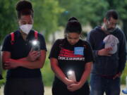 Naiyolis Paloma, center, prays with others during a community vigil for the dozens of people found dead Monday in a semitrailer containing suspected migrants as well as those who received heat related injuries, Tuesday, June 28, 2022, in San Antonio. Due to a flame ban, the group used artificial candles and cell phones.