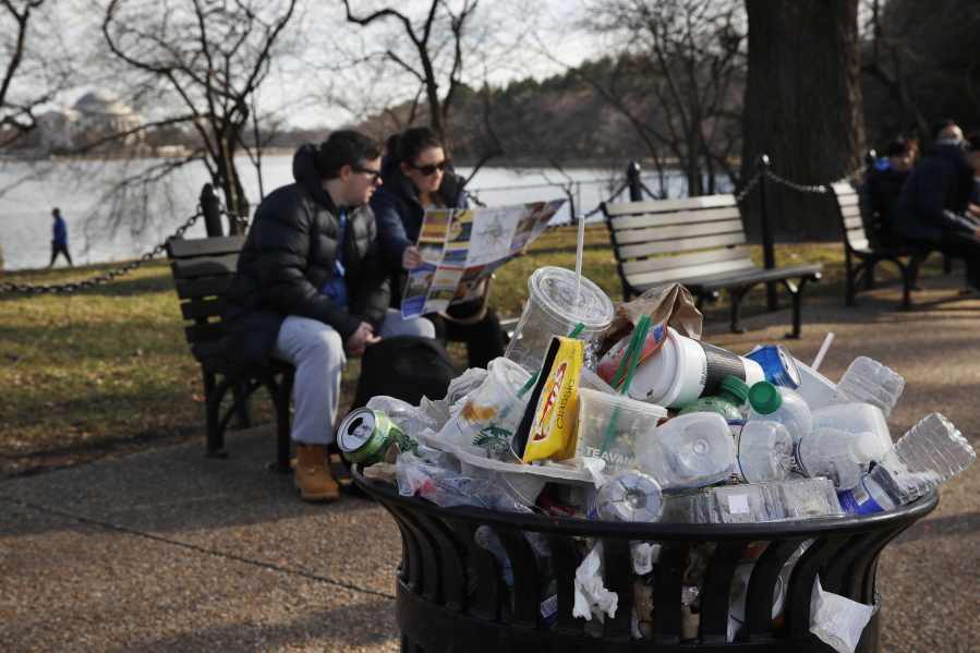 FILE - A trash can overflows as people sit outside of the Martin Luther King Jr. Memorial by the Tidal Basin, Dec. 27, 2018, in Washington, during a partial government shutdown. The Interior Department said Wednesday, June 8, 2022, it will phase out single-use plastic products on national parks and other public lands over the next decade, targeting a leading source of U.S.