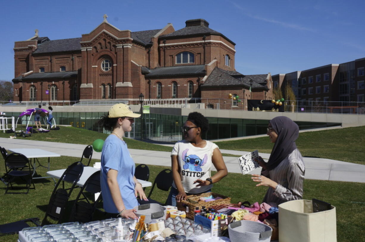 From left, University of St. Thomas students Helen Knudson, Arianna Norals, and Salma Nadir set up a table for decorating mason jars and headscarves at the school's celebration for the end of the Muslim holy month of Ramadan on the lawn in front of the Catholic chapel in St. Paul, Minn., on Saturday, May 7, 2022. Campus ministry helped organize the event, which included similar stress-reducing activities, as many faith leaders across US campuses seek ways to help students manage stress and anxiety.