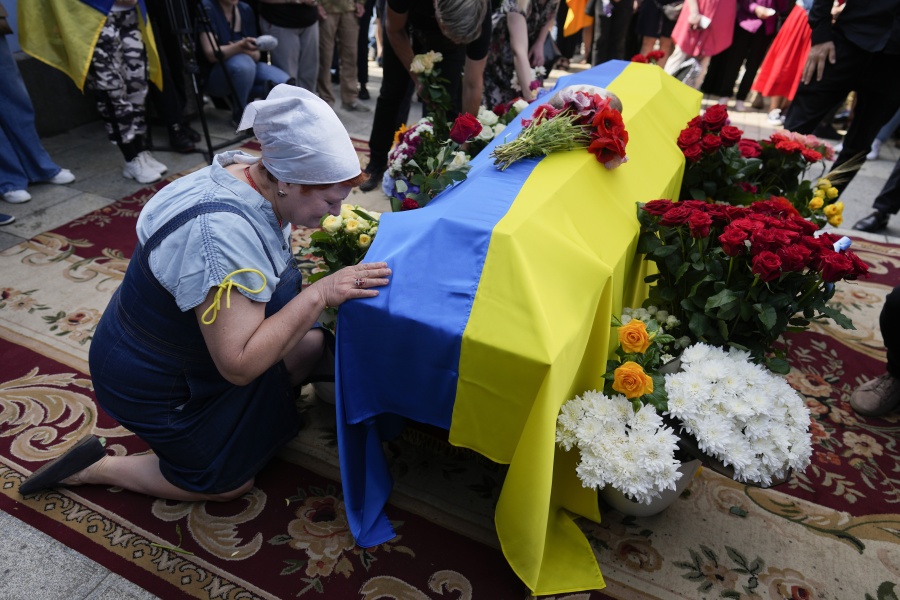 A woman kneels at activist and soldier Roman Ratushnyi's coffin during his memorial service in Kyiv, Ukraine, Saturday, June 18, 2022. Ratushnyi died in a battle near Izyum, where Russian and Ukrainian troops are fighting for control of the area.