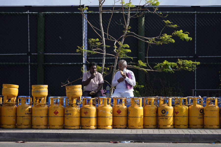People eat their breakfast while sitting by a line of empty gas canisters that are placed outside the Galle International Cricket Stadium, the venue for the test cricket matches between Australia and Sri Lanka, in Galle, Sri Lanka, Tuesday, June 28, 2022.