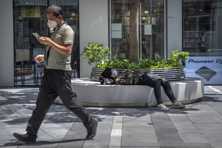 A man wearing a face mask takes a nap at a shopping and office complex in Beijing, Wednesday, June 1, 2022.