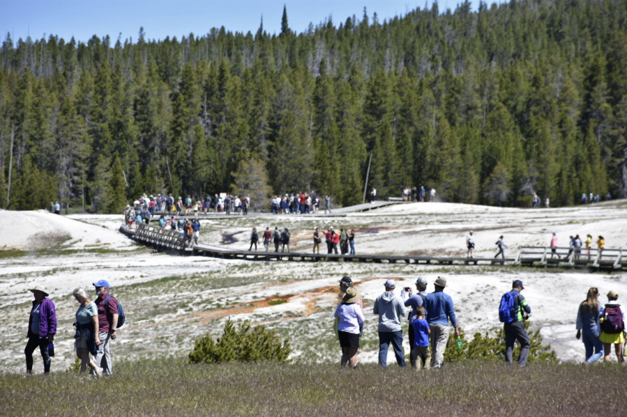 FILE - Tourists walk along a boardwalk in Upper Geyser Basin on June 22, 2022, in Yellowstone National Park, Wyo. The park is reopening its flood-damaged north loop at noon on Saturday, July 2, 2022, in time for the Fourth of July holiday weekend. Park officials say the roads from Norris Junction to Mammoth Hot Springs, to Tower-Roosevelt, to Canyon Junction and back to Norris Junction will be open.