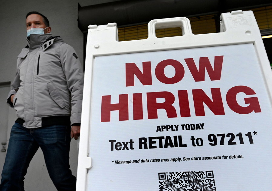 A man wearing a face mask walks past a "Now Hiring" sign in front of a store on Jan. 13, 2022, in Arlington, Virginia.