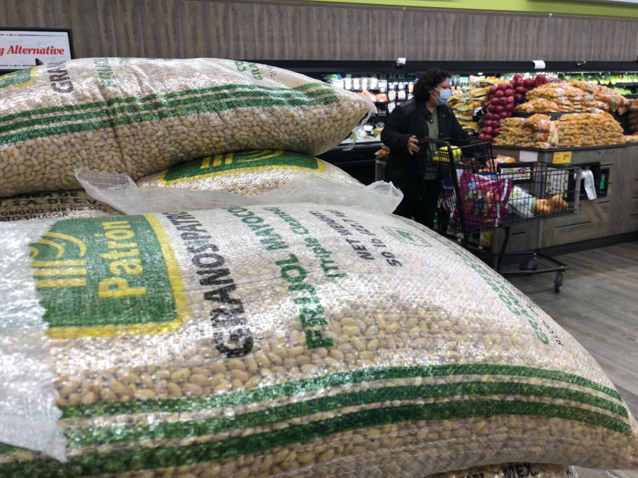 Bags selling beans are fully stocked while a woman shops for produce wearing a mask at a Vons in Los Feliz on April 7, 2020, in Los Angeles, California. Signs around the store announce purchase limit, social distancing guidelines and that no returns are accepted.