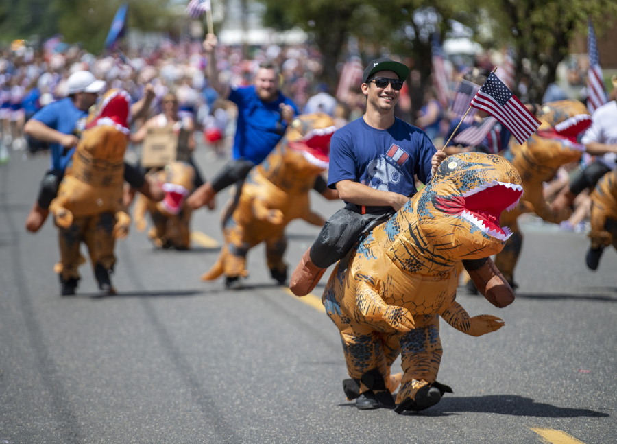 People in inflatable dinosaur costumes march down Pioneer Street on Monday, July 4, 2022, during a Fourth of July parade in downtown Ridgefield.
