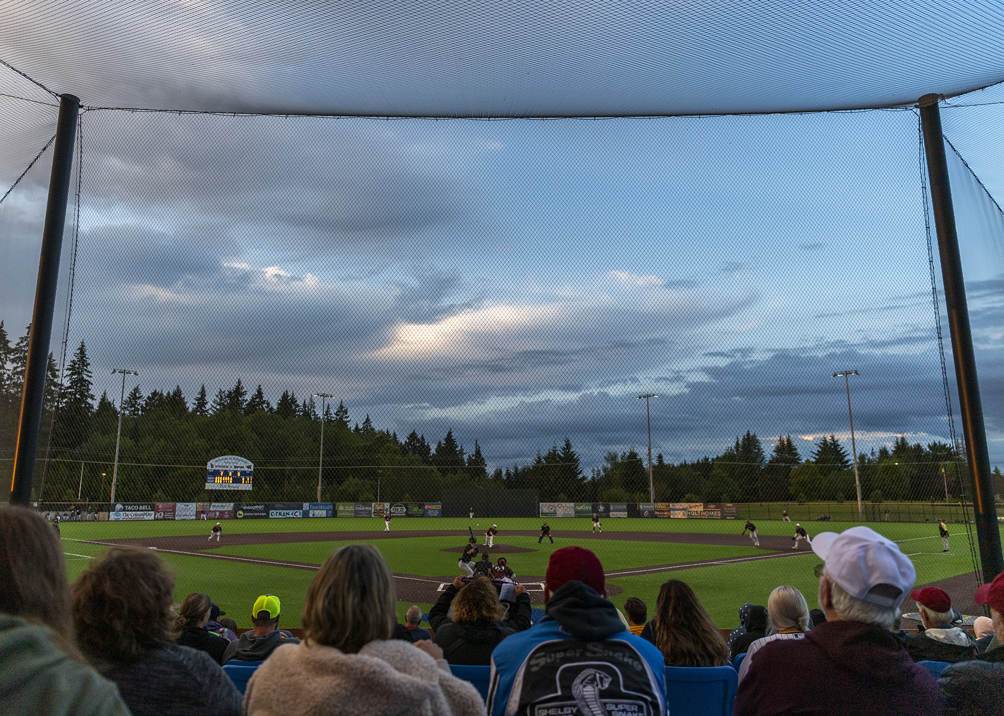 Fans watch a baseball game between the Ridgefield Raptors and the Corvallis Knights under partly cloudy skies Wednesday, July 6, 2022, at the Ridgefield Outdoor Recreation Complex.