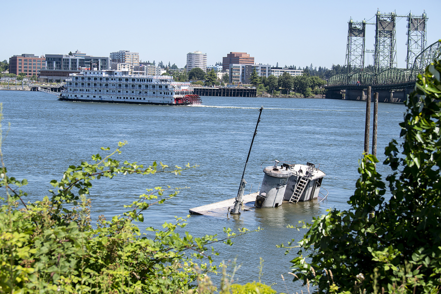 An abandoned ship, foreground, is seen in the Columbia River near Jantzen Beach, Ore., as the American Pride riverboat cruises past Vancouver.