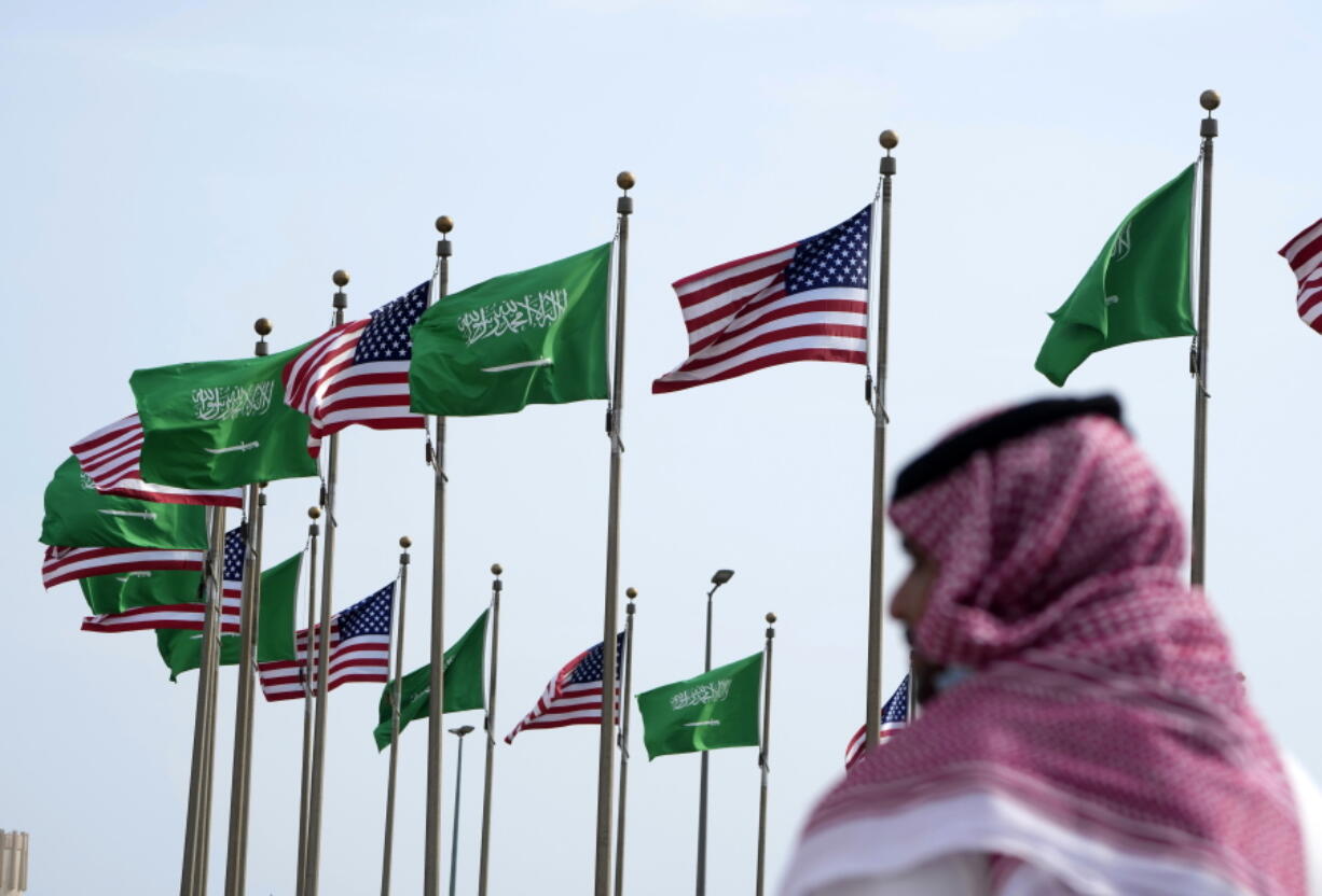 FILE - A man stands under American and Saudi Arabian flags prior to a visit by U. S. President Joe Biden, at a square in Jeddah, Saudi Arabia, Thursday, July 14, 2022. As President Joe Biden prepares to meet Saudi Crown Prince Mohammed bin Salman on Friday, the prince's reputation as a brazen leader whose rise to power coincided with a sweeping crackdown on critics will likely cast a shadow on the meeting.