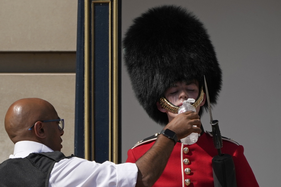 A police officer givers water to a British soldier wearing a traditional bearskin hat, on guard duty outside Buckingham Palace, during hot weather in London, Monday, July 18, 2022. The British government have issued their first-ever "red" warning for extreme heat. The alert covers large parts of England on Monday and Tuesday, when temperatures may reach 40 degrees Celsius (104 Fahrenheit) for the first time, posing a risk of serious illness and even death among healthy people, the U.K. Met Office, the country's weather service, said Friday.