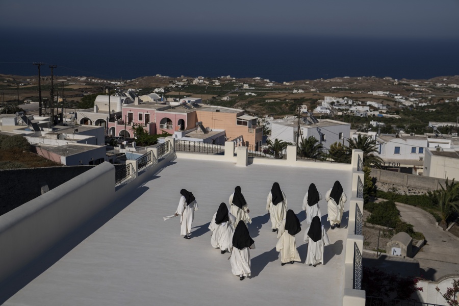 Cloistered nuns walk on a terrace of the Catholic Monastery of St. Catherine on the Greek island of Santorini on Tuesday, June 14, 2022. Twice a day, the nuns recess to chat on the convent's wide terraces, the Aegean Sea shimmering in the distance.