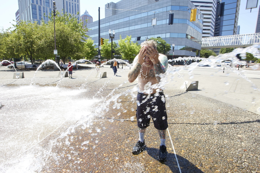 Matthew Carr cools off in the Salmon Street Springs fountain before returning to work cleaning up trash on his bicycle in Portland, Ore., Tuesday, July 26, 2022.