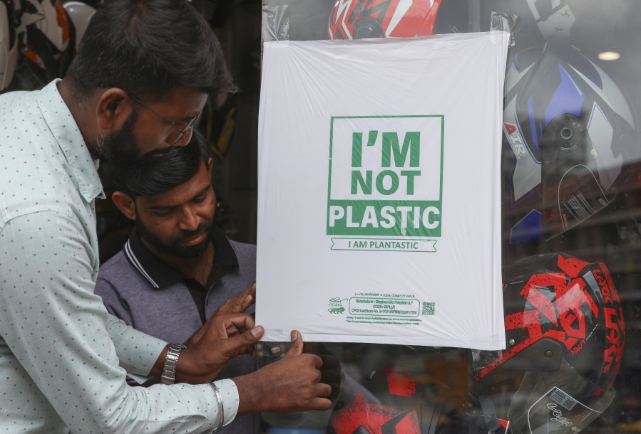 Workers of a helmet store paste degradable plastic substitute material on a glass in Hyderabad, India, Thursday, June 30, 2022. India banned some single-use or disposable plastic products Friday as a part of a longer federal plan to phase out the ubiquitous material in the nation of nearly 1.4 billion people.