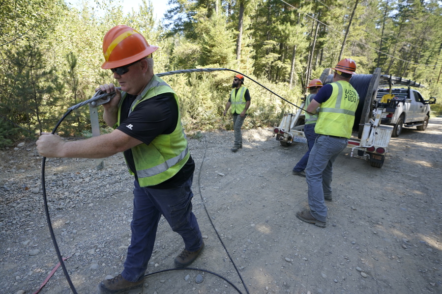 Carl Roath, left,  with the Mason County Public Utility District, pulls fiber optic cable off a spool as he works with a team to install broadband internet service to homes in a rural area surrounding Lake Christine near Belfair, Wash., on Aug. 4, 2021.
