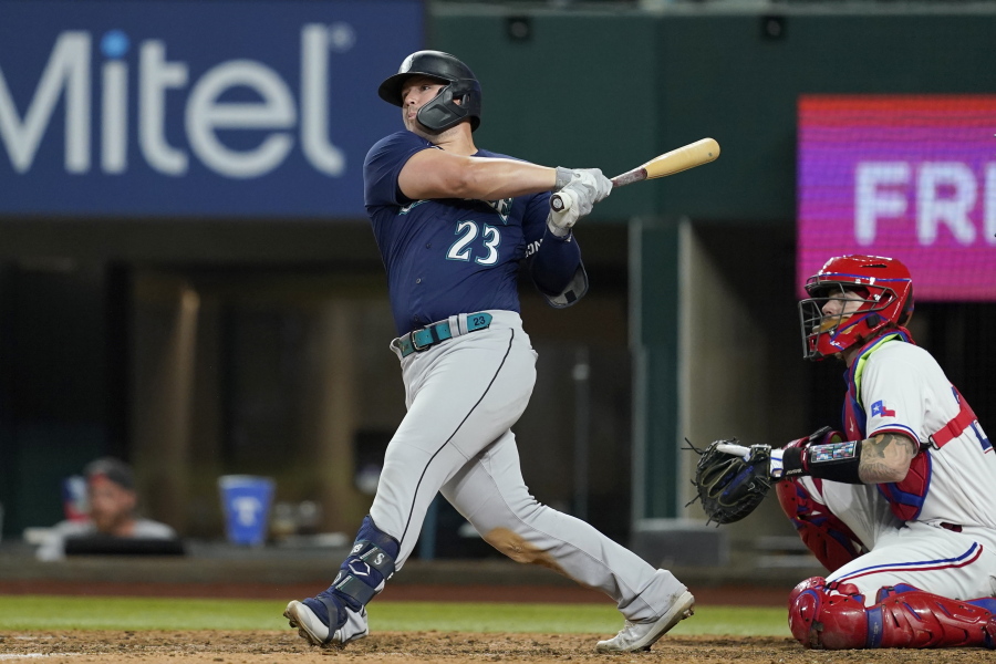 Seattle Mariners' Ty France follows through on a two-run single next to Texas Rangers catcher Jonah Heim during the eighth inning of a baseball game Thursday, July 14, 2022, in Arlington, Texas.