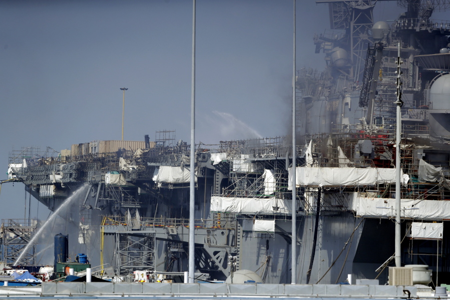 FILE - Fire crews spray water from the dock onto the side of the USS Bonhomme Richard, in San Diego, July 12, 2020. Navy leaders have disciplined more than 20 senior officers and sailors in connection with widespread leadership and other failures that contributed to the July 2020 arson fire that destroyed the USS Bonhomme Richard.