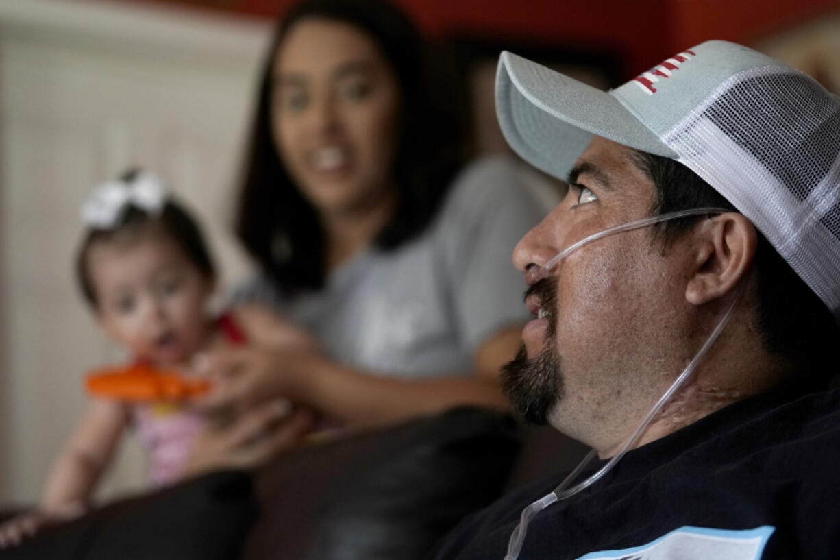 Freddy Fernandez sits with his fianc?, Vanessa Cruz, and their 8-month-old daughter, Mariana Fernandez in their home Friday, June 10, 2022, in Carthage, Mo. After contracting COVID-19 in August 2021, Fernandez spent months hooked up to a respirator and an ECMO machine before coming home in February 2022 to begin his long recovery from the disease.