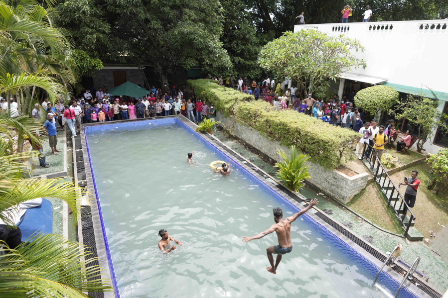 Protesters swim as onlookers wait at a swimming pool in president's official residence a day after it was stormed in Colombo, Sri Lanka, Sunday, July 10, 2022. Sri Lanka's opposition political parties will meet Sunday to agree on a new government a day after the country's president and prime minister offered to resign in the country's most chaotic day in months of political turmoil, with protesters storming both officials' homes and setting fire to one of the buildings in a rage over the nation's economic crisis.