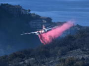 FILE - A plane drops retardant on a wildfire near homes Thursday, Feb. 10, 2022, in Laguna Beach, Calif. U.S. officials are testing a new wildfire retardant after two decades of buying millions of gallons annually from one supplier, but watchdogs say the expensive strategy is overly fixated on aerial attacks at the expense of hiring more fire-line digging ground crews.  (AP Photo/Ringo H.W.