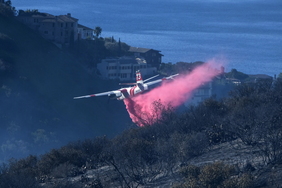 FILE - A plane drops retardant on a wildfire near homes Thursday, Feb. 10, 2022, in Laguna Beach, Calif. U.S. officials are testing a new wildfire retardant after two decades of buying millions of gallons annually from one supplier, but watchdogs say the expensive strategy is overly fixated on aerial attacks at the expense of hiring more fire-line digging ground crews.  (AP Photo/Ringo H.W.