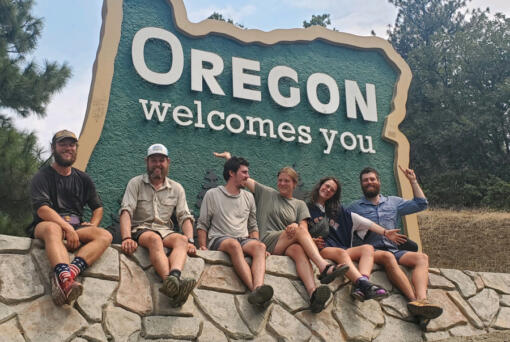 Pacific Crest Trail hikers pose in front of the Oregon Welcomes You sign after crossing into Oregon from California.