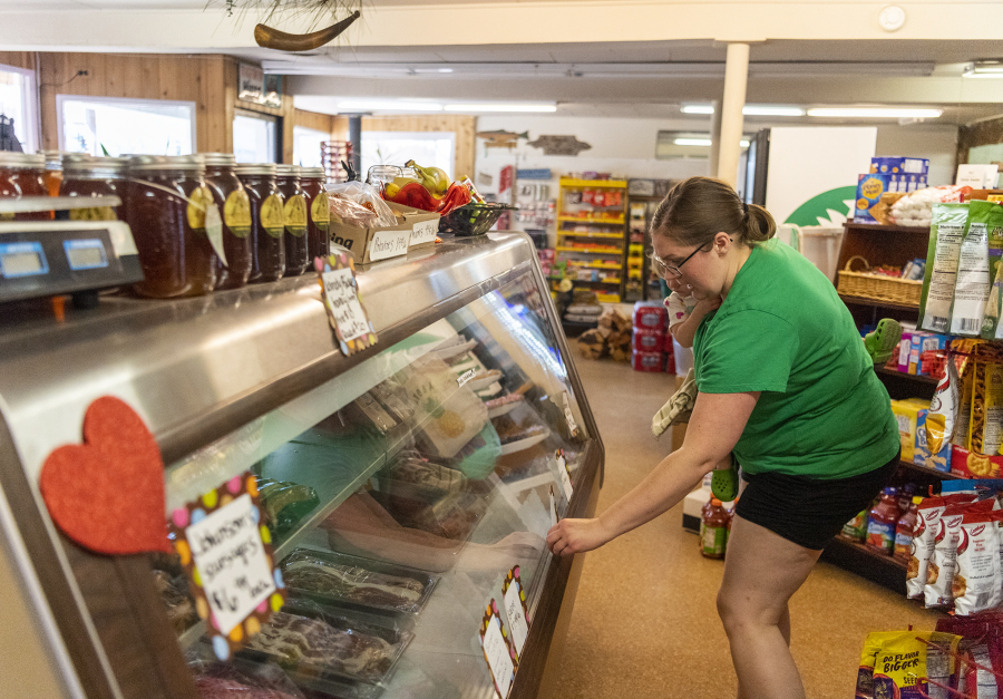 Owner Jenell Anderson, right, holds her daughter, Nora Einarson, 1, and adjusts a sign on a meat cooler at the Heisson Store in Battle Ground.