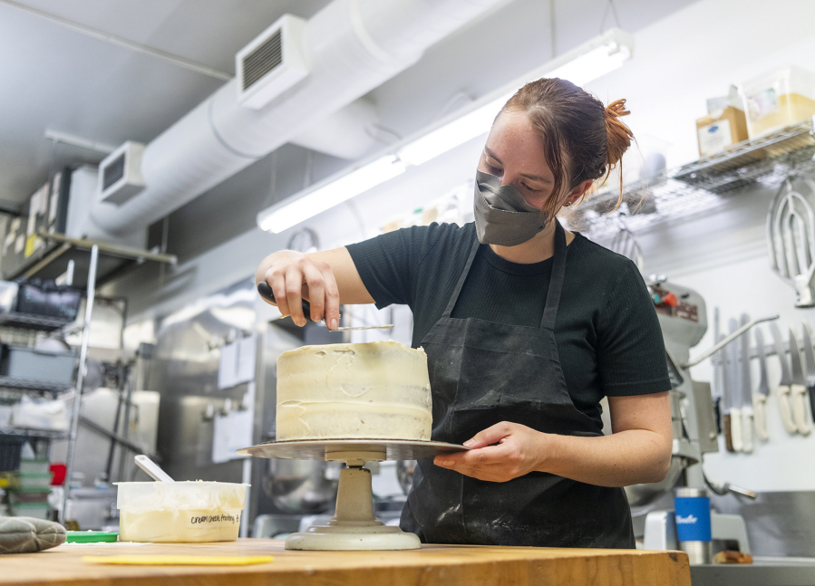 Karalee Tittle spreads cream cheese frosting on a carrot cake at Bleu Door Bakery in Vancouver's Uptown Village. Inflation has increased the price of baking goods like flour, eggs and butter.