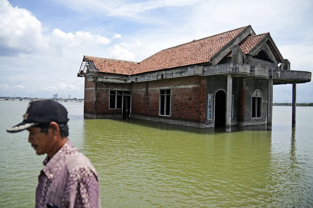 FILE - A man walks past a house abandoned after it was inundated by water due to the rising sea level in Sidogemah, Central Java, Indonesia, Nov. 8, 2021. Climate hazards such as flooding, heat waves and drought have worsened more than half of the hundreds of known infectious diseases in people, such as malaria, hantavirus, cholera and even anthrax, according to a new study released Monday, Aug. 8, 2022.