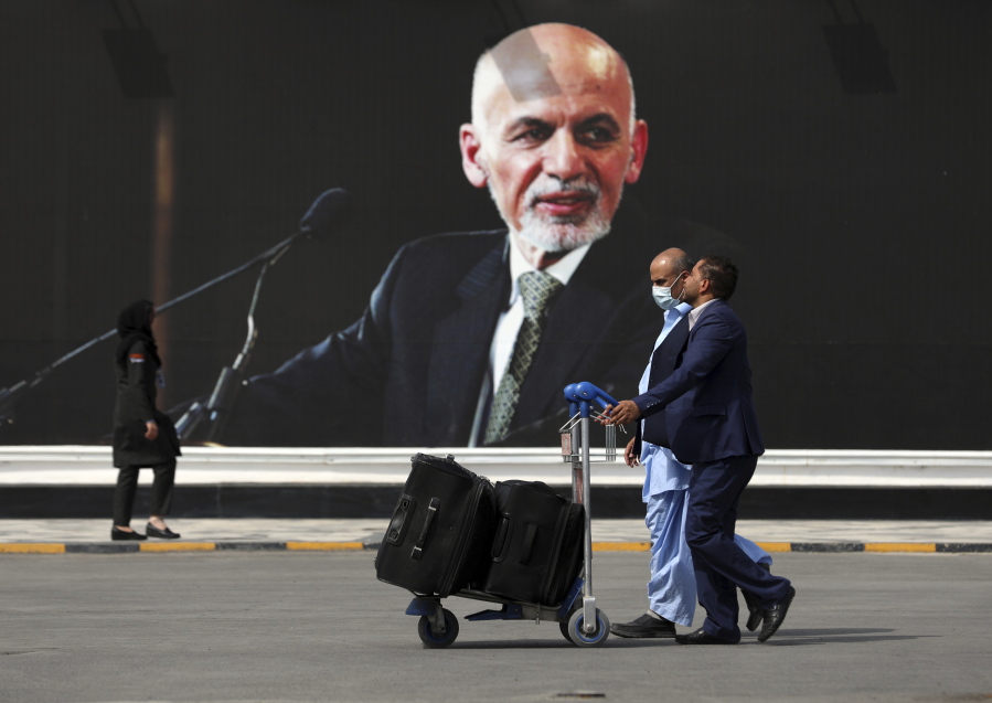 FILE - Passengers walk to the departures terminal of Hamid Karzai International Airport in Kabul, Afghanistan, on Saturday, Aug. 14, 2021, past a mural of President Ashraf Ghani, as the Taliban offensive encircled the capital. On the eve of the anniversary of the Taliban takeover of Kabul, Afghanistan's former president on Sunday, Aug. 14, 2022, defended what he said was a split-second decision to flee, saying he wanted to avoid the humiliation of surrender to the insurgents.