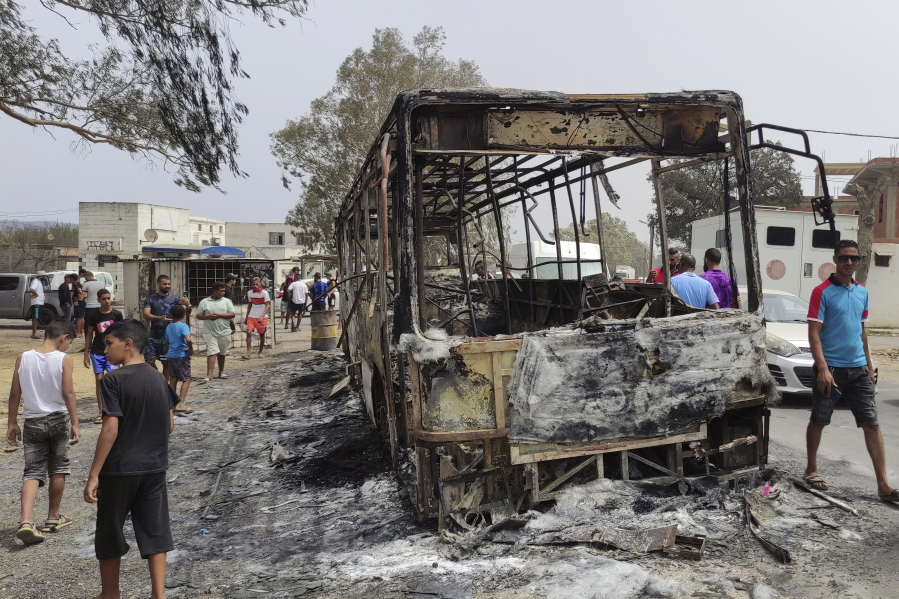 Residents walk past a charred truck in El Kala, in the El Tarf region, near the northern Algerian-Tunisian border, Thursday, Aug.18, 2022. Wildfires raging in the forests of eastern Algeria have killed at least 26 people, according to a "provisional report" by the north African country's interior minister.
