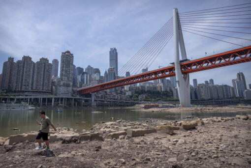 A man walks along the lower than normal bank of the Jialing River in southwestern China's Chongqing Municipality, Friday, Aug. 19, 2022. Ships crept down the middle of the Yangtze on Friday after the driest summer in six decades left one of the mightiest rivers shrunk to barely half its normal width and set off a scramble to contain damage to a weak economy in a politically sensitive year.