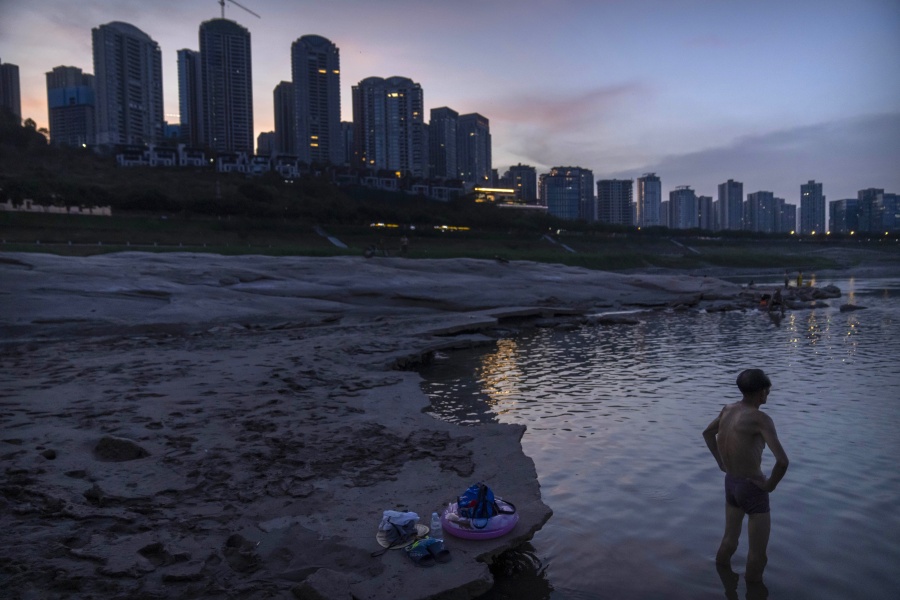 A man stands in shallow water near the dry riverbed of the Yangtze River in southwestern China's Chongqing Municipality, Friday, Aug. 19, 2022. Ships crept down the middle of the Yangtze on Friday after the driest summer in six decades left one of the mightiest rivers shrunk to barely half its normal width and set off a scramble to contain damage to a weak economy in a politically sensitive year.