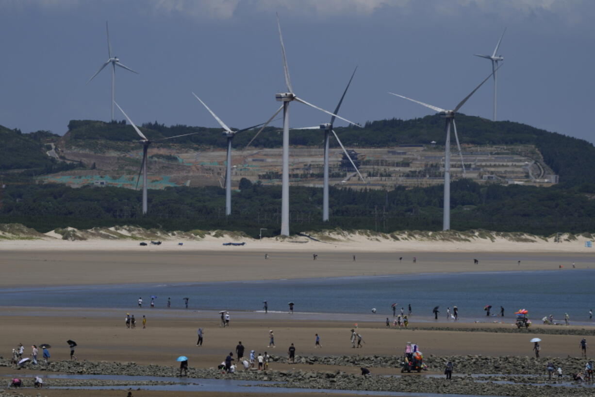 Beachgoers walk near wind turbines along the coast of Pingtan in Southern China's Fujian province, on Aug. 6, 2022. The world's two biggest emitters of greenhouse gases are sparring on Twitter over climate policy, with China asking if the U.S. can deliver on the landmark climate legislation signed into law by President Joe Biden this week.