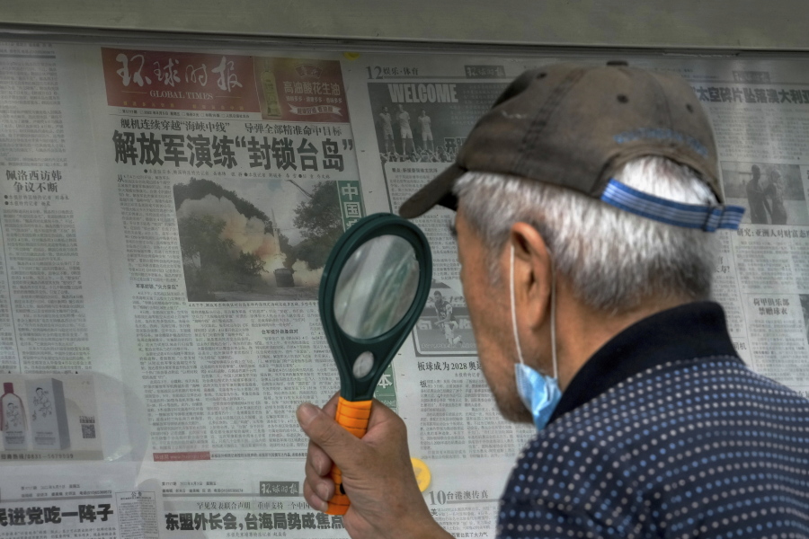 A man uses a magnifying glass to read a newspaper headline reporting on Chinese People's Liberation Army (PLA) conducting military exercises, at a stand in Beijing, Sunday, Aug. 7, 2022. U.S. Secretary of State Antony Blinken said Saturday that China should not hold hostage talks on important global matters such as the climate crisis, after Beijing cut off contacts with Washington in retaliation for U.S. House Speaker Nancy Pelosi's visit to Taiwan earlier this week.