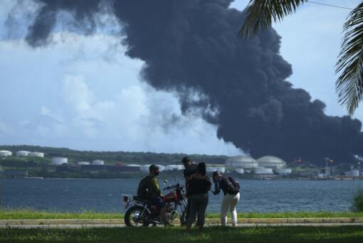 People watch a huge rising plume of smoke from the Matanzas Supertanker Base, as firefighters try to quell a blaze which began during a thunderstorm the night before, in Matazanas, Cuba, Saturday, Aug. 6, 2022. Cuban authorities say lightning struck a crude oil storage tank at the base, causing a fire that led to four explosions which injured more than 50 people.