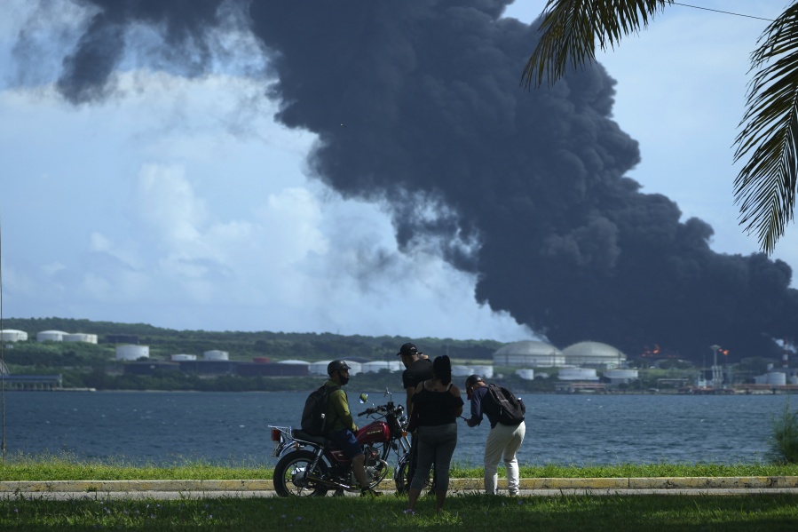People watch a huge rising plume of smoke from the Matanzas Supertanker Base, as firefighters try to quell a blaze which began during a thunderstorm the night before, in Matazanas, Cuba, Saturday, Aug. 6, 2022. Cuban authorities say lightning struck a crude oil storage tank at the base, causing a fire that led to four explosions which injured more than 50 people.