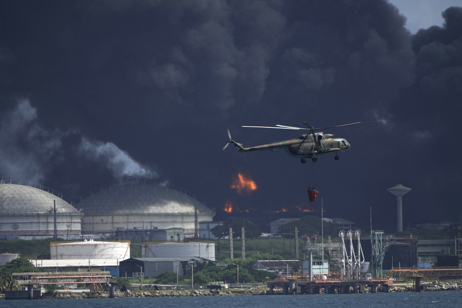A helicopter carrying water flies over the Matanzas Supertanker Base, as firefighters try to quell the blaze which began during a thunderstorm the night before, in Matazanas, Cuba, Saturday, Aug. 6, 2022. Cuban authorities say lightning struck a crude oil storage tank at the base, causing a fire that led to four explosions which injured more than 50 people.