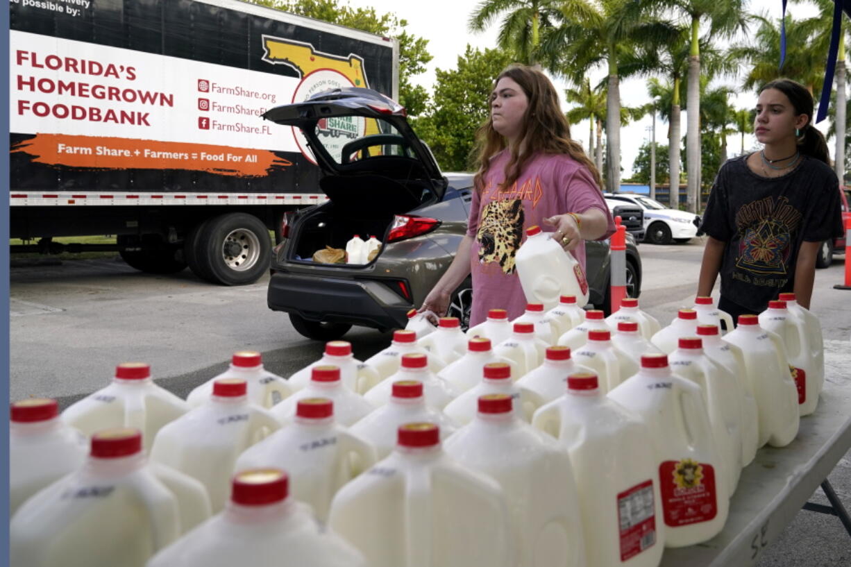 Vanessa Correa, left, and Gigi Fiske, right, pass out gallons of milk at a food distribution held by the Farm Share food bank, Wednesday, July 20, 2022, in Miami. Long lines are back at food banks around the U.S. as working Americans overwhelmed by inflation turn to handouts to help feed their families.