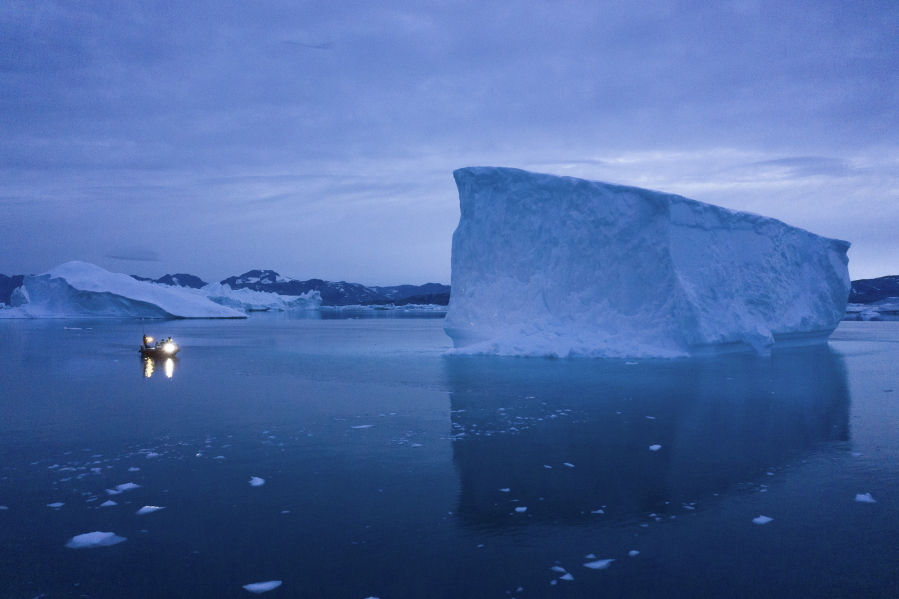 FILE - A boat navigates at night next to large icebergs in eastern Greenland on Aug. 15, 2019. Zombie ice from the massive Greenland ice sheet will eventually raise global sea level by at least 10 inches (27 centimeters) on its own, according to a study released Monday, Aug. 29, 2022.  Zombie or doomed ice is still attached to thicker areas of ice, but it's no longer getting fed by those larger glaciers.