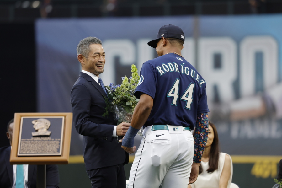 Former Seattle Mariners player Ichiro Suzuki, left, is presented with a bouquet of flowers by Mariners' Julio Rodriguez as he is inducted into the Mariners Hall of Fame during a ceremony before a baseball game between the Mariners and the Cleveland Guardians, Saturday, Aug. 27, 2022, in Seattle.