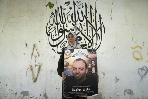 Palestinian Dalal Awawdeh poses with a poster of her husband Khalil Awawdeh, who is a prisoner in Israel, at the family house, in the West Bank village of Idna, Hebron, Tuesday, Aug. 9, 2022. Awawdeh, who is on a protracted hunger strike, was moved Thursday from an Israeli jail to a hospital because of his worsening condition, the prisoner's wife said.