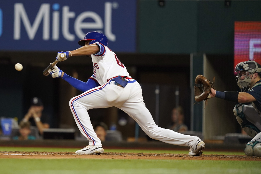 Texas Rangers' Bubba Thompson, left, hits a sacrifice bunt in front of Seattle Mariners catcher Cal Raleigh during the fourth inning of a baseball game in Arlington, Texas, Saturday, Aug. 13, 2022. Rangers' Charlie Culberson scored on the play.